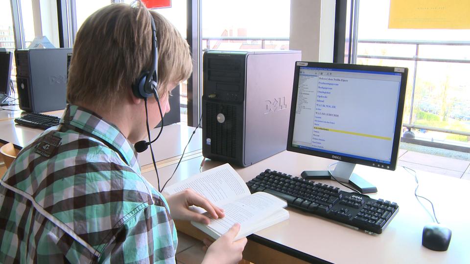Een jongen luistert met de AMIS-software naar een Daisy-boek op zijn computer. Hij leest tegelijkertijd mee in het gedrukte boek.